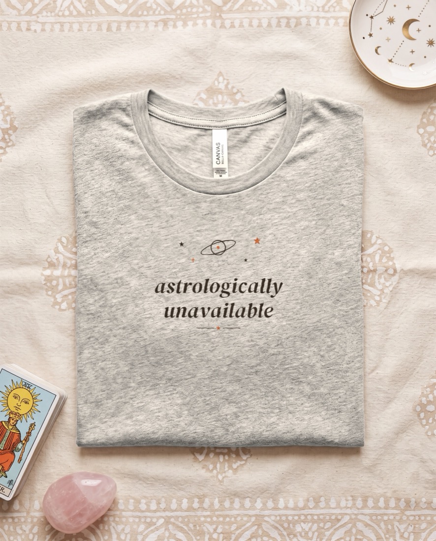 Astrologically Unavailable tee, folded on a brand backdrop