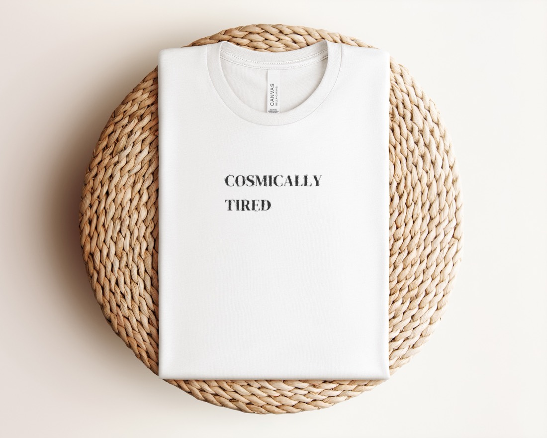 White Cosmically Tired tee folded on a woven mat
