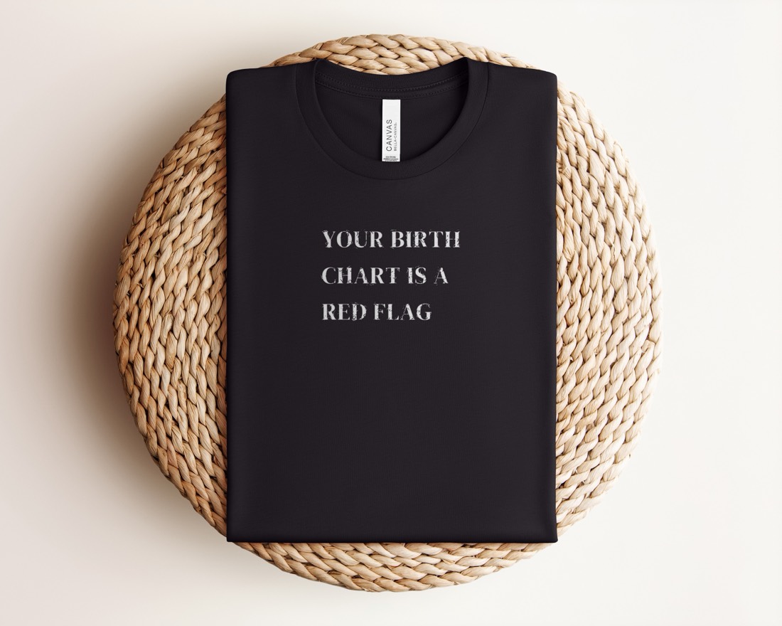 Black Your Birth Chart Is A Red Flag tee folded on a woven mat